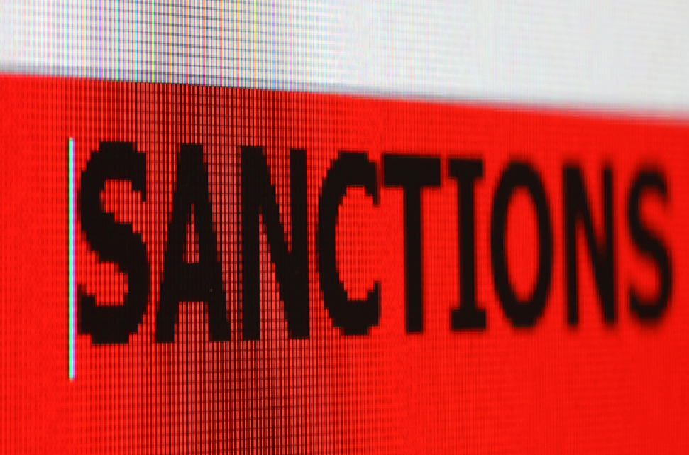 A close-up of a computer screen with the word "Sanctions" in black text on a red background.