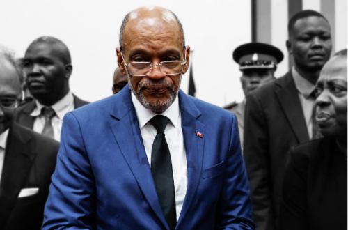 A man in a suit and tie, identified as Prime Minister Ariel Henry of Haiti, is standing in front of a group of people.