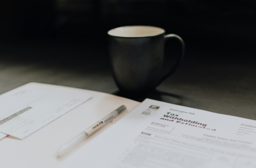 A focused workspace featuring tax paperwork, a pen, and a steaming cup of coffee on a desk, suggesting a moment of financial organization and tax filing preparation.