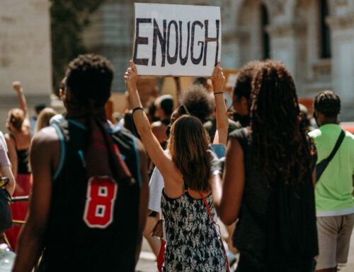 A diverse group of students at a protest against student debt with one individual prominently holding up a sign that reads 