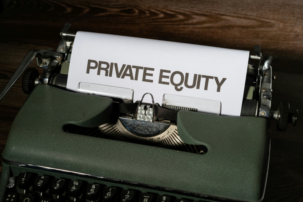A vintage typewriter with a sheet of paper displaying the text "PRIVATE EQUITY" in reference to private equity in health care. The typewriter is positioned on a wooden surface, giving a rustic and classic feel to the image.