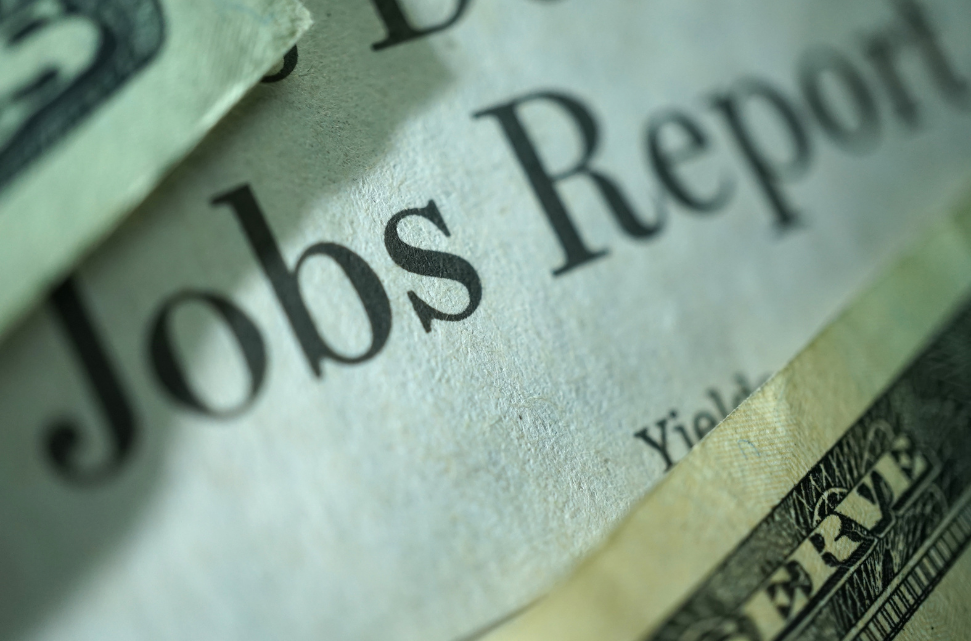 Close-up of a newspaper with the headline "August Jobs Report," partially covered by a stack of U.S. bills.