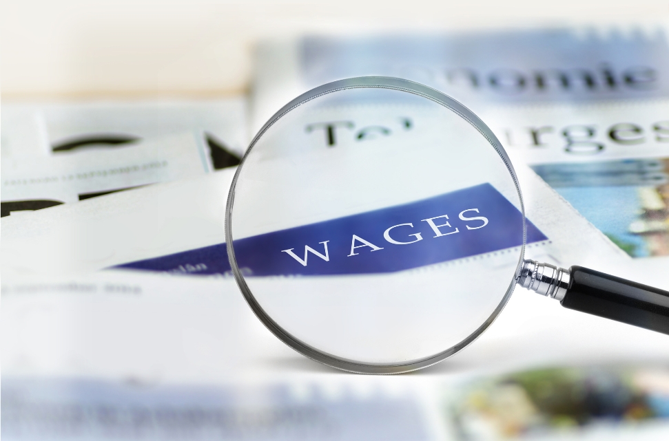 A magnifying glass focuses on the word "WAGES" on a newspaper, highlighting the text among other blurred headlines.