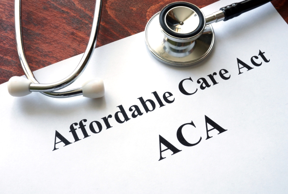 A stethoscope rests on a document titled "Affordable Care Act (ACA)" on a wooden surface.