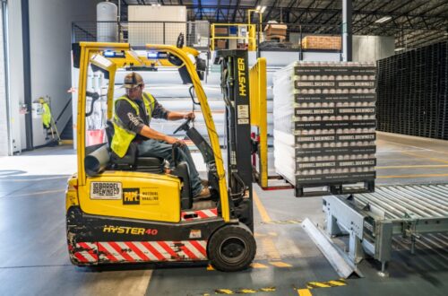 A man operating a forklift inside a warehouse, efficiently moving goods among shelves and storage areas.