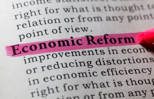 A close-up of a hand holding a marker, writing on a piece of paper filled with text about economic reform and efficiency.