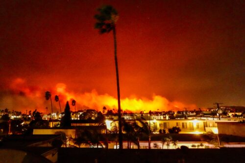 Flames illuminate the night sky as a wildfire burns across a hillside in Pacific Palisades, California, on January 7, 2025. The most destructive fires in Los Angeles history kill at least five people, destroy thousands of structures, and force approximately 180,000 people to evacuate. (Photo by Jason Ryan/NurPhoto via Getty Images)