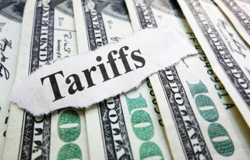 A visual representation of tariffs, highlighting the tax levied on imports and its impact on trade dynamics. The torn bill sits on top of several hundred dollar bills.