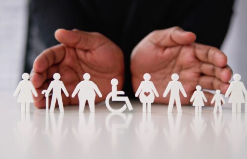 Two outstretched hands highlighting multiple paper cutouts of women, children and people with disabilities.