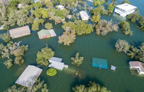 Aerial view of a flooded neighborhood with partially submerged houses and trees, surrounded by water.