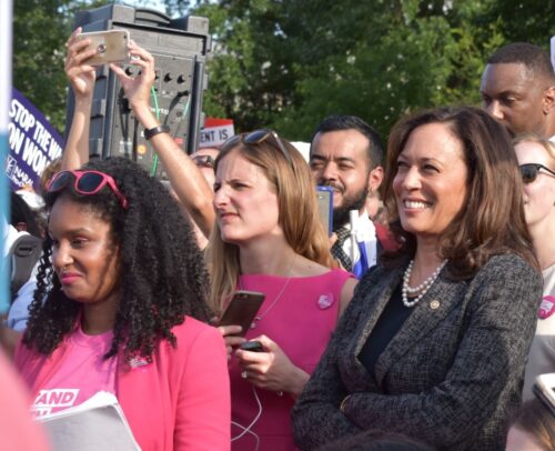 Kamala Harris at protest surrounded by men and women, many wearing pink t-shirts.