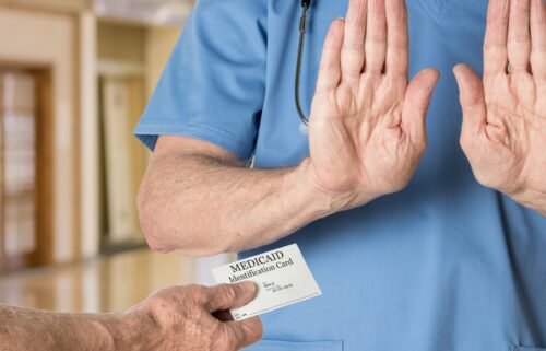 A doctor is holding his hands up, refusing to accept a patients Medicaid identification card as a form of payment.