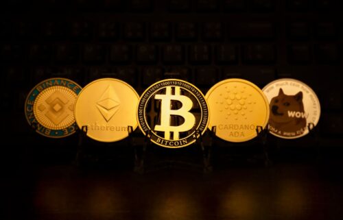 A circle of gold bitcoins arranged together, reflecting light against a dark background, showcasing their metallic shine. The coins have various inscriptions and symbols visible on their surfaces.