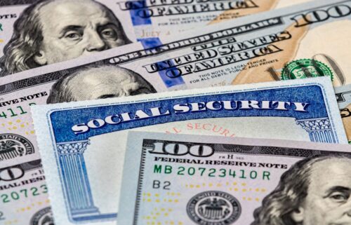 A close-up image of a Social Security card partially covering several U.S. one-hundred-dollar bills. The blue and white card displays the words Social Security prominently. The bills show partial images of Benjamin Franklin and intricate security features.