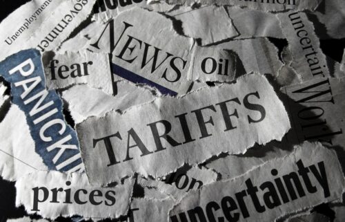 Torn newspaper headlines scattered, reading “Panic,” “Tariffs,” “Fear,” and “Uncertainty,” conveying a chaotic and anxious tone. Dark, somber lighting.
