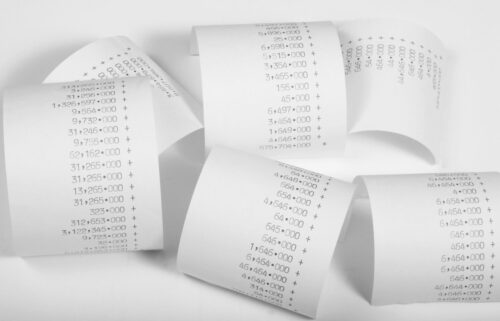 Curled rolls of receipt paper with large printed numbers and plus signs on a white background, conveying a sense of finance and accounting.