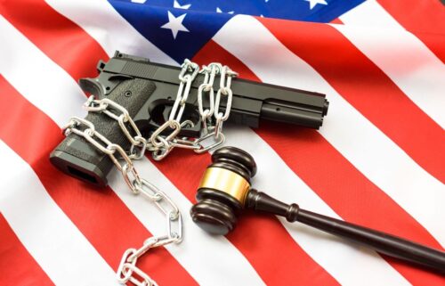 A handgun wrapped in chains lies on an American flag, symbolizing gun control. A judge's gavel rests nearby, highlighting legal authority.
