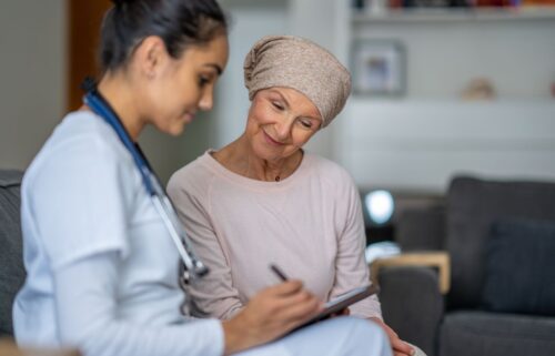 A nurse with a stethoscope consults a woman in a headscarf. They are in a comfortable setting, reviewing medicaid and medicare options.