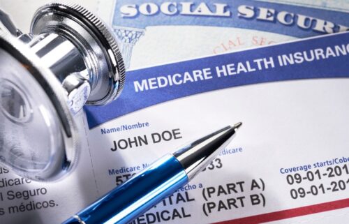 A close-up of a Medicare health insurance card and Social Security card, partially covered by a stethoscope and pen. The image suggests healthcare and insurance themes.