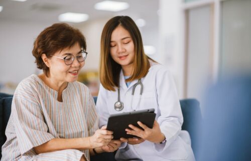 A doctor and a patient sitting together, smiling as they discuss information on a tablet. The setting is bright and friendly, conveying a supportive tone.