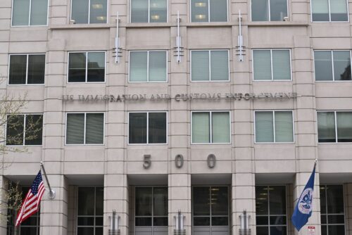 Immigration and Customs Enforcement (ICE) building with flags and name above the entrance. 500 12th Street SW, Washington, DC 20536.