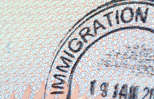 Close-up of an immigration stamp on a passport page, featuring interlaced red and blue patterns. The word 