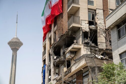 Sanctions Watch June 2025: TEHRAN, IRAN - JUNE 25: An Iranian flag is draped from a building damaged during a recent attack by Israel near Milad Tower in Tehran, Iran, on June 25, 2025. The ceasefire that began on June 24 appears to be in effect between Iran and Israel. The two countries had exchanged missile fire daily for almost two weeks after Israel launched a preemptive strike on Iran's nuclear program, military leadership, and other locations starting from June 13. (Photo by Majid Saeedi/Getty Images)