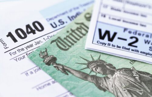 Tax forms, including 1040 and W-2, overlap with a green paper featuring the Statue of Liberty. The image conveys the theme of taxes and finance.