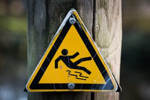 Yellow triangular warning sign on a wooden post, showing a stick figure slipping. Highlights caution for slippery surfaces. Foreboding and alerting tone.