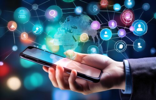 Hand holding a smartphone with a glowing digital world map background. Icons and connections symbolize global communication, social media, and technology.