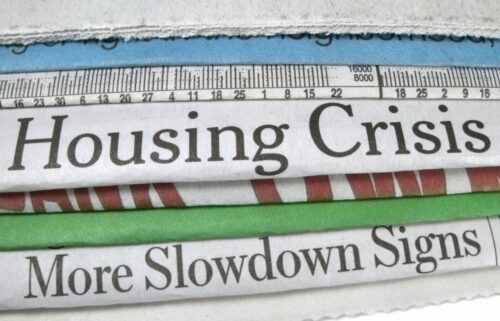 Stack of newspapers displaying headlines about the housing crisis and economic slowdown, emphasizing current issues in real estate.