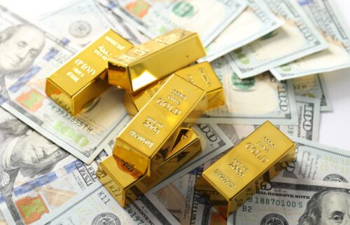 Stacks of gold bars are scattered atop numerous U.S. 100 dollar bills, symbolizing wealth and investment.