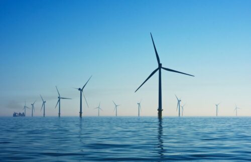 Offshore wind farm with multiple turbines standing in calm ocean water under a clear blue sky, conveying a sense of renewable energy.