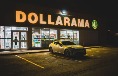 A sleek silver car is parked in front of a brightly lit Dollarama store at night. The warm glow from the sign casts a cozy ambiance on the empty parking lot.