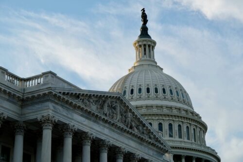 Dome of the US Capitol building under a blue sky with soft clouds. The marble structure and columns exude grandeur and historical significance.