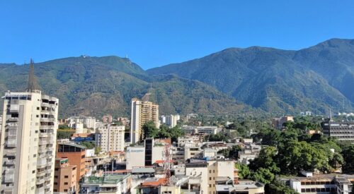 Cerro El Ávila - Caracas. Cityscape view with tall buildings in the foreground and lush, green mountains in the background under a clear blue sky.