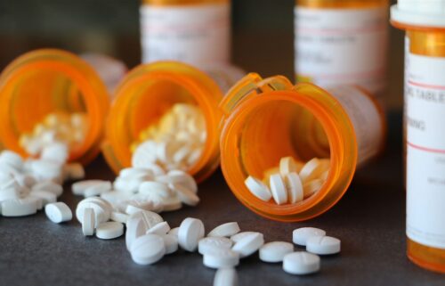 Prescription bottles lie on their sides, with white pills spilling out onto a dark surface, conveying a sense of carelessness or urgency.