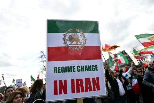 An anti-Iranian regime protester hold a placard picturing the Iranian flag before the 1979 revolution with the Lion and Sun emblems and reading a message asking for a change of regime, during a march in support of the US and Israel attack on Iran and the killing of Iran's supreme leader, in Paris on March 1, 2026. Iranian state television confirmed the death of Iran's supreme leader Ayatollah Ali Khamenei on February 28, 2026, after US President said he had been killed. The announcement came after the United States and Israel started launching waves of strikes against targets in Iran, sparking swift retaliation by the Islamic republic. (Photo by Anna KURTH / AFP via Getty Images)