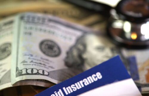 A stethoscope lies on a partially blurred stack of hundred-dollar bills and a document labeled 