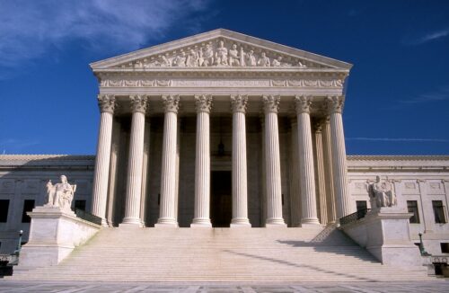The Supreme Court of the United States building, featuring its iconic columns and pediment against a clear blue sky.