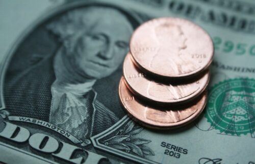 Stack of three US pennies on a dollar bill, featuring George Washington's portrait.