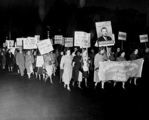 Crowd carrying placards and a banner reading, 