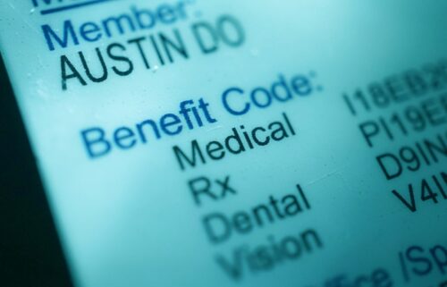 Close-up of a health insurance card showing “Member: AUSTIN DO” and “Benefit Code: Medical, Rx, Dental, Vision” on a light blue background.