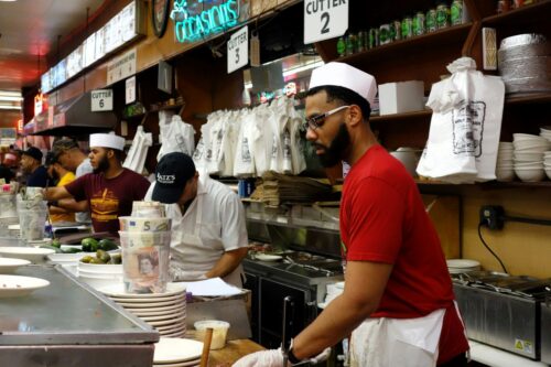 A man wearing a red shirt works at a restaurant counter, illustrating the challenges of income volatility for shift workers.