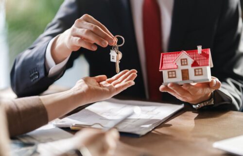 A realtor presents house keys to a woman, marking the completion of a property sale.